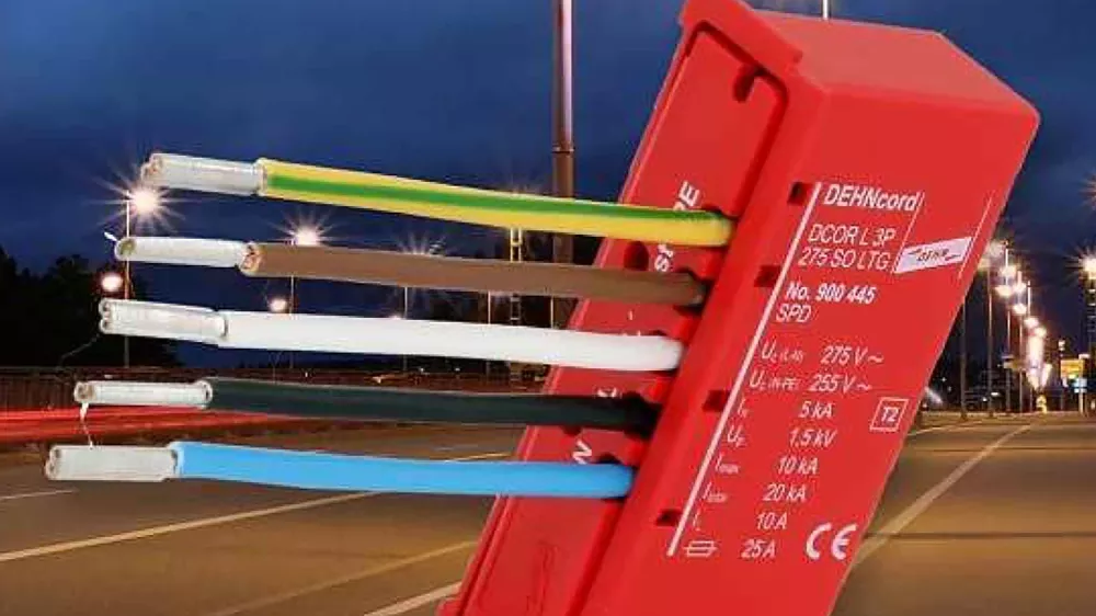 Red surge protection device with multiple colored wires connected, shown against a nighttime street with illuminated streetlights.