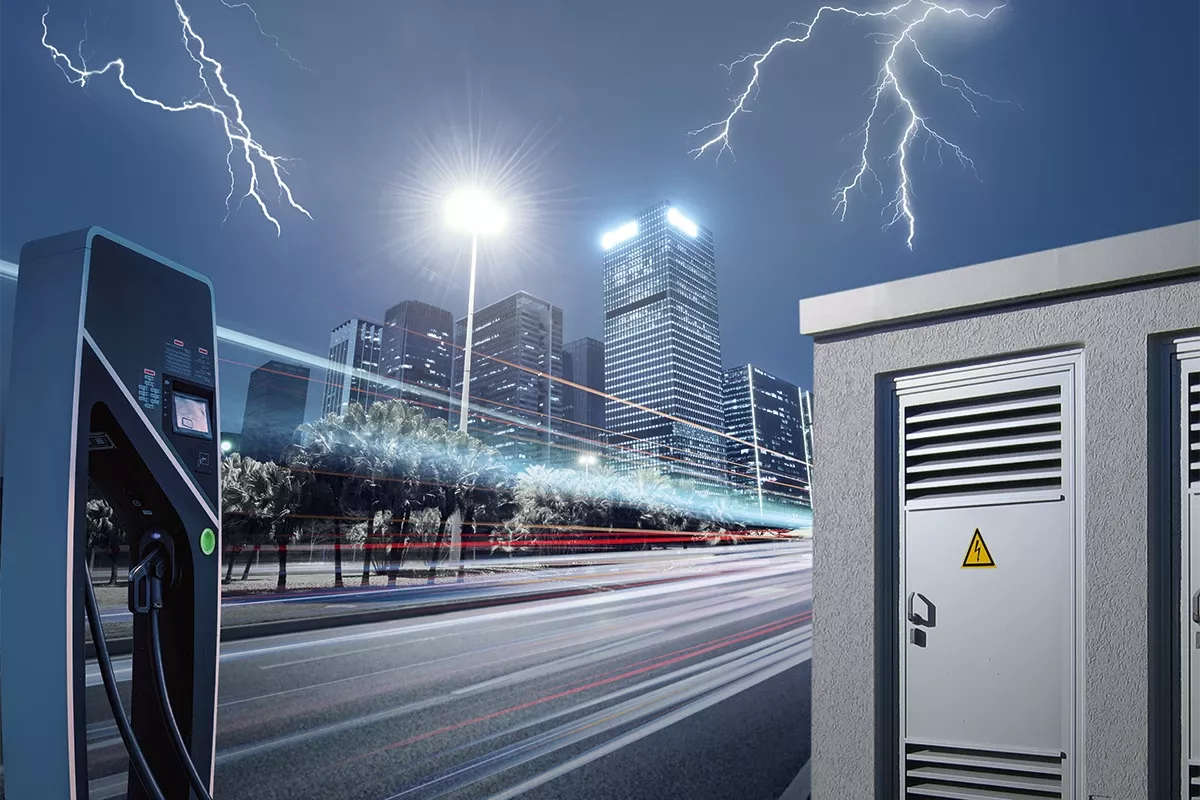 Electric vehicle charging station and power cabinet in an urban setting at night, with lightning over a city skyline.